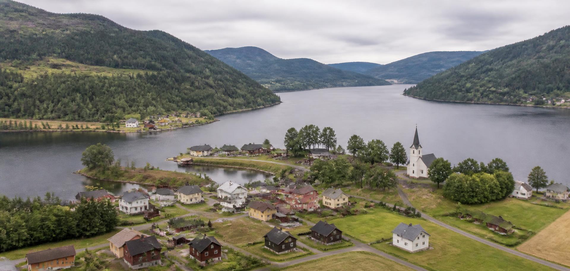 Utsyn over ei roleg bygd ved eit vatn med skogkledde fjell i Vest-Telemark